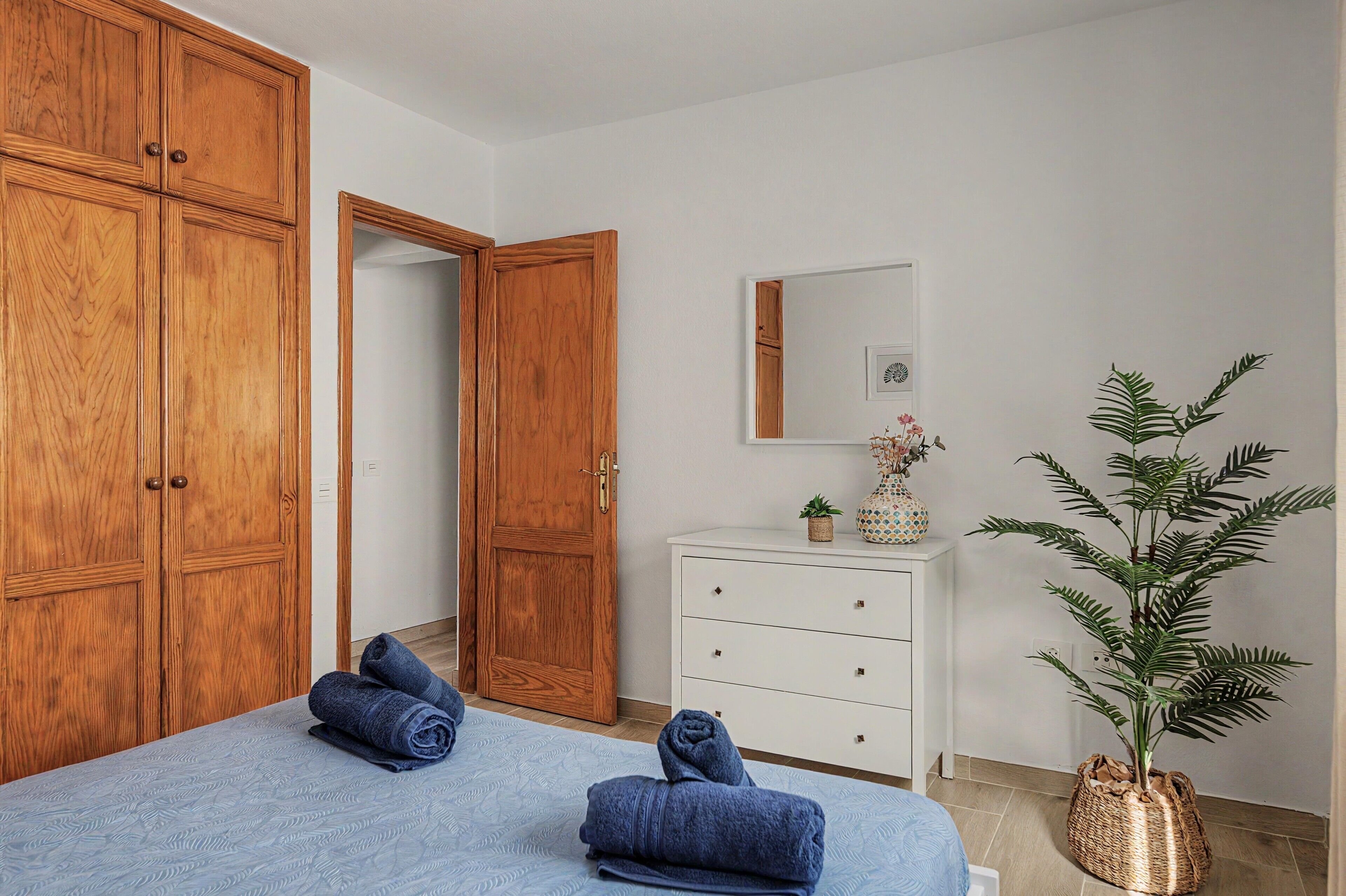 Une chambre à coucher comprenant un lit, une armoire, une commode, un miroir et une plante en pot.