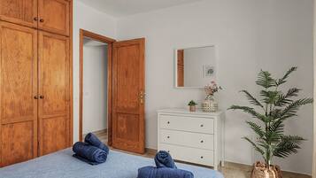 Un dormitorio con cama, armario, tocador, espejo y planta en maceta.