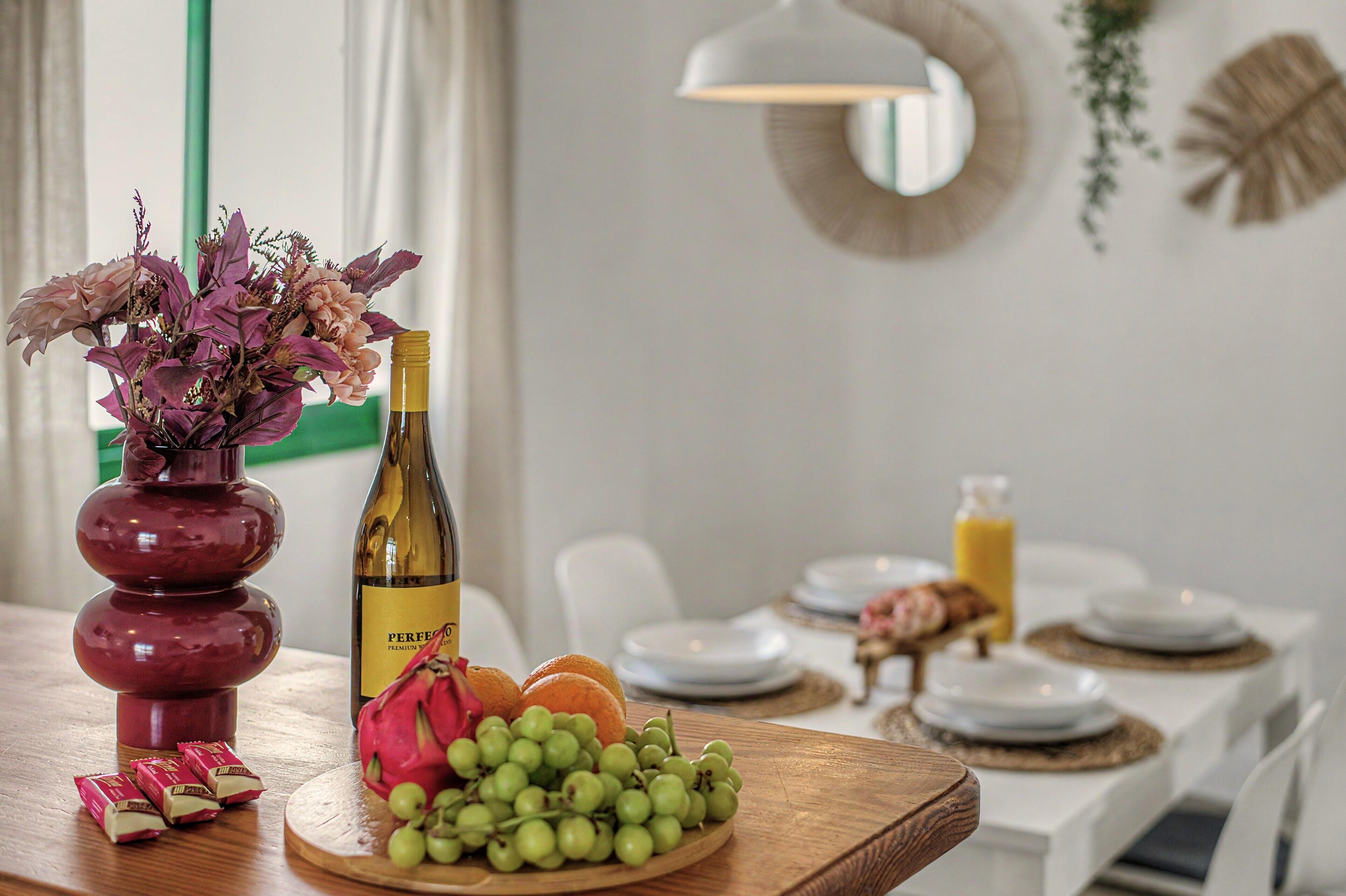 Een eettafel met een wijnfles, een fruitschaal en een bloevas.