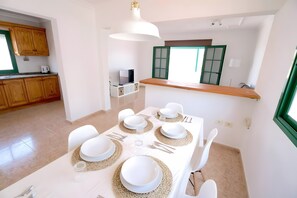 A dining area with a table set for six, a TV in the background, and wooden cabinets.