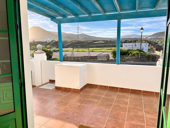 A balcony with a view of a mountainous landscape, a tiled floor, and a blue ceiling.
