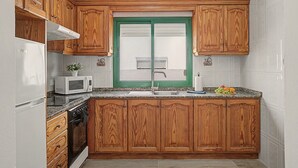 A kitchen with wooden cabinets, a white refrigerator, a microwave, a stove, and a green-framed window.