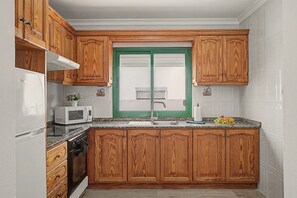 A kitchen with wooden cabinets, a white refrigerator, a microwave, a stove, and a green-framed window.