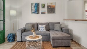 A living room with a grey sectional sofa, a small round side table, and a floor lamp. There are three framed artworks on the wall above the sofa.