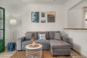 A living room with a grey sectional sofa, a small round side table, and a floor lamp. There are three framed artworks on the wall above the sofa.