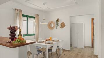A dining area with a white table set for four, chairs, a vase with flowers, and a bottle of wine.