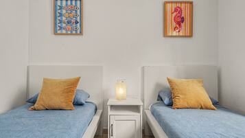 Une chambre avec deux lits, chacun recouvert d’une couverture à motifs bleus et agrémenté d’un oreiller marron. Une petite table de chevet avec une lampe se trouve entre les deux lits.