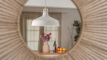 Quarto com um espelho redondo refletindo um candeeiro pendente, um vaso com flores e uma cesta de frutas.