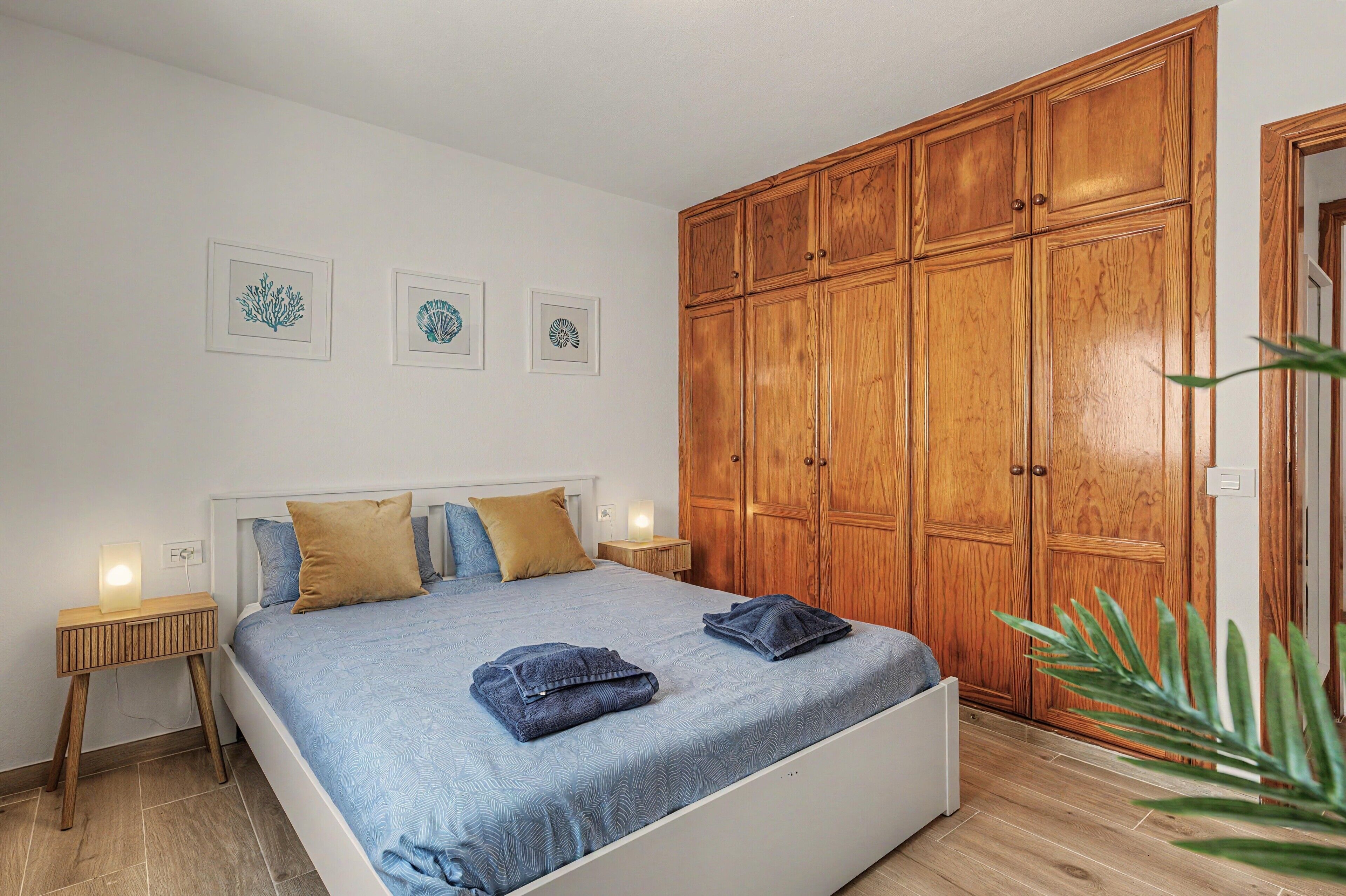 A bedroom with a bed, wooden wardrobe, bedside tables, and framed artwork on the wall.