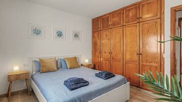 A bedroom with a bed, wooden wardrobe, bedside tables, and framed artwork on the wall.