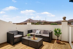 A rooftop terrace with a sofa, two chairs, a small table, and a potted plant.