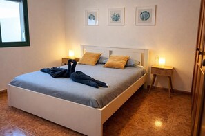 A neatly made bed with towels, a bedside table, a nightstand, and framed artwork on the wall.