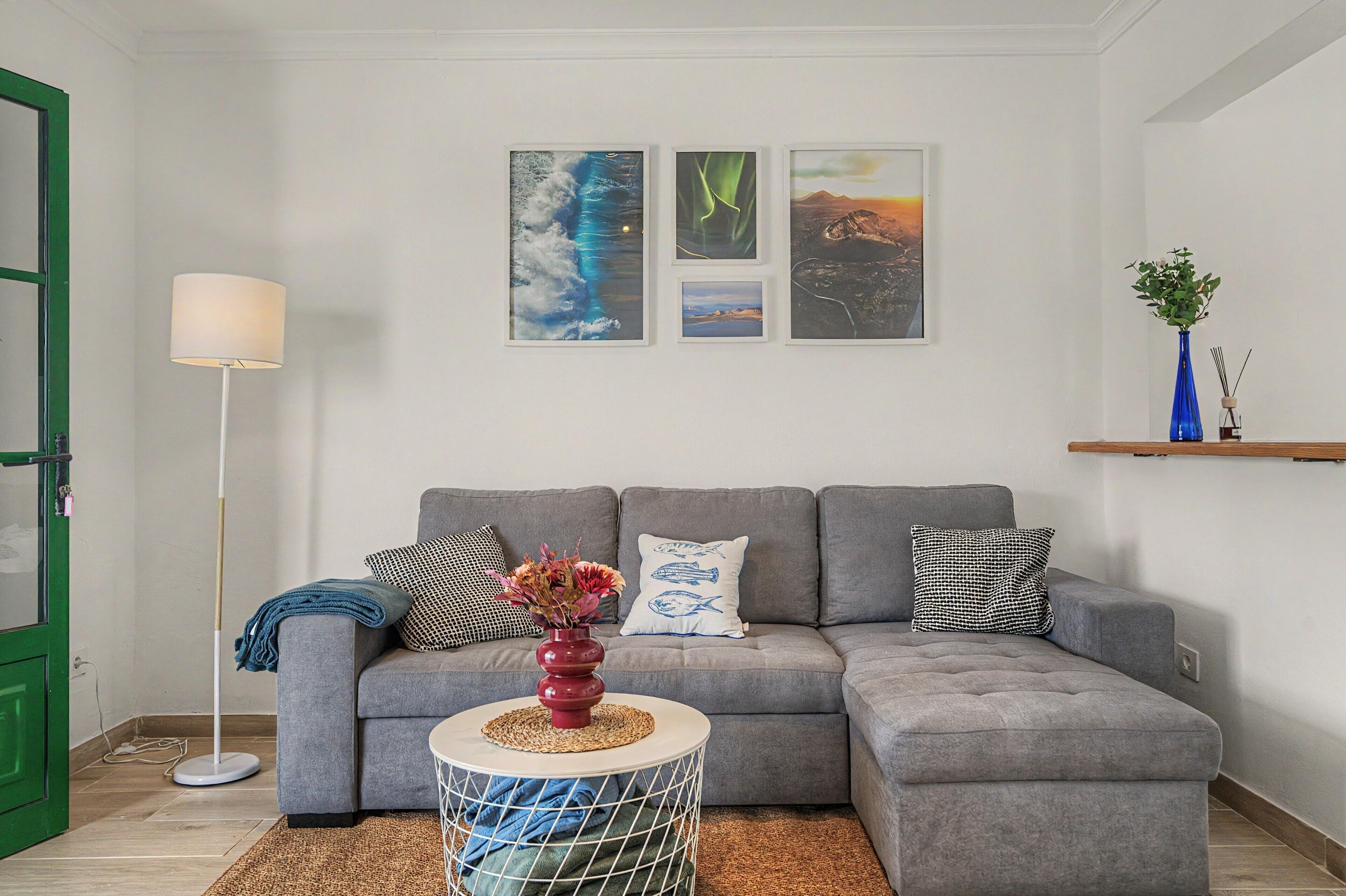 A living room with a grey sectional sofa, a small round table with a vase, and three framed artworks on the wall.