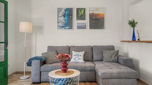 Un salon avec un canapé d’angle gris, une petite table ronde surmontée d’un vase et trois œuvres d’art encadrées accrochées au mur.