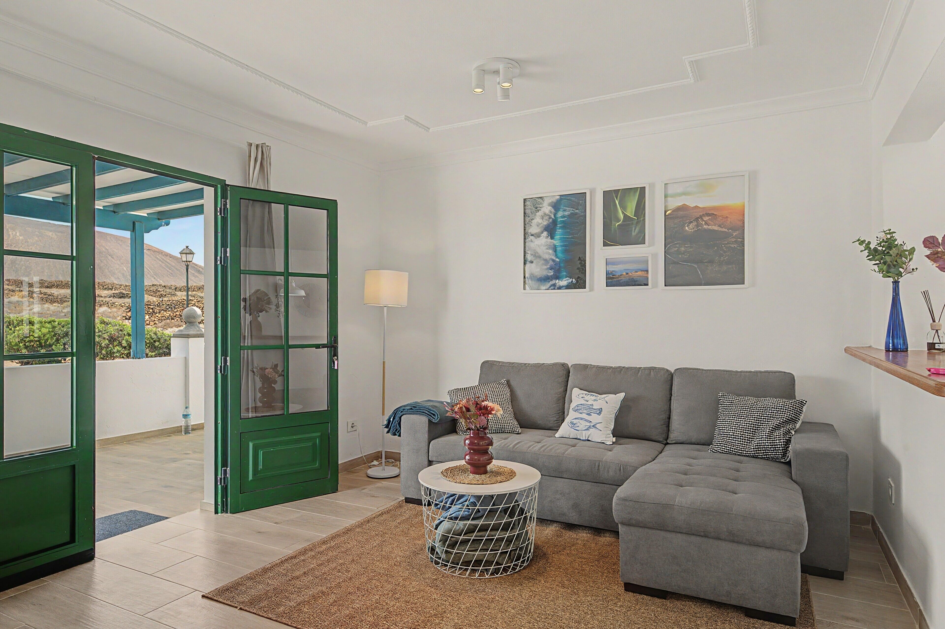 Uma sala de estar moderna com um sofá cinzento, uma mesa de centro e uma porta verde que dá para uma área externa.