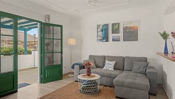 Uma sala de estar moderna com um sofá cinzento, uma mesa de centro e uma porta verde que dá para uma área externa.