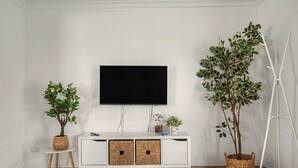 Un salon moderne avec un téléviseur à écran plat fixé au mur, un meuble de rangement blanc doté de deux portes et deux plantes en pot.