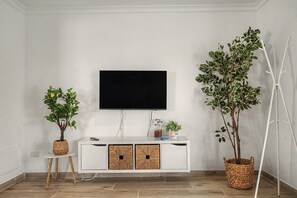 Un salon moderne avec un téléviseur à écran plat fixé au mur, un meuble de rangement blanc doté de deux portes et deux plantes en pot.
