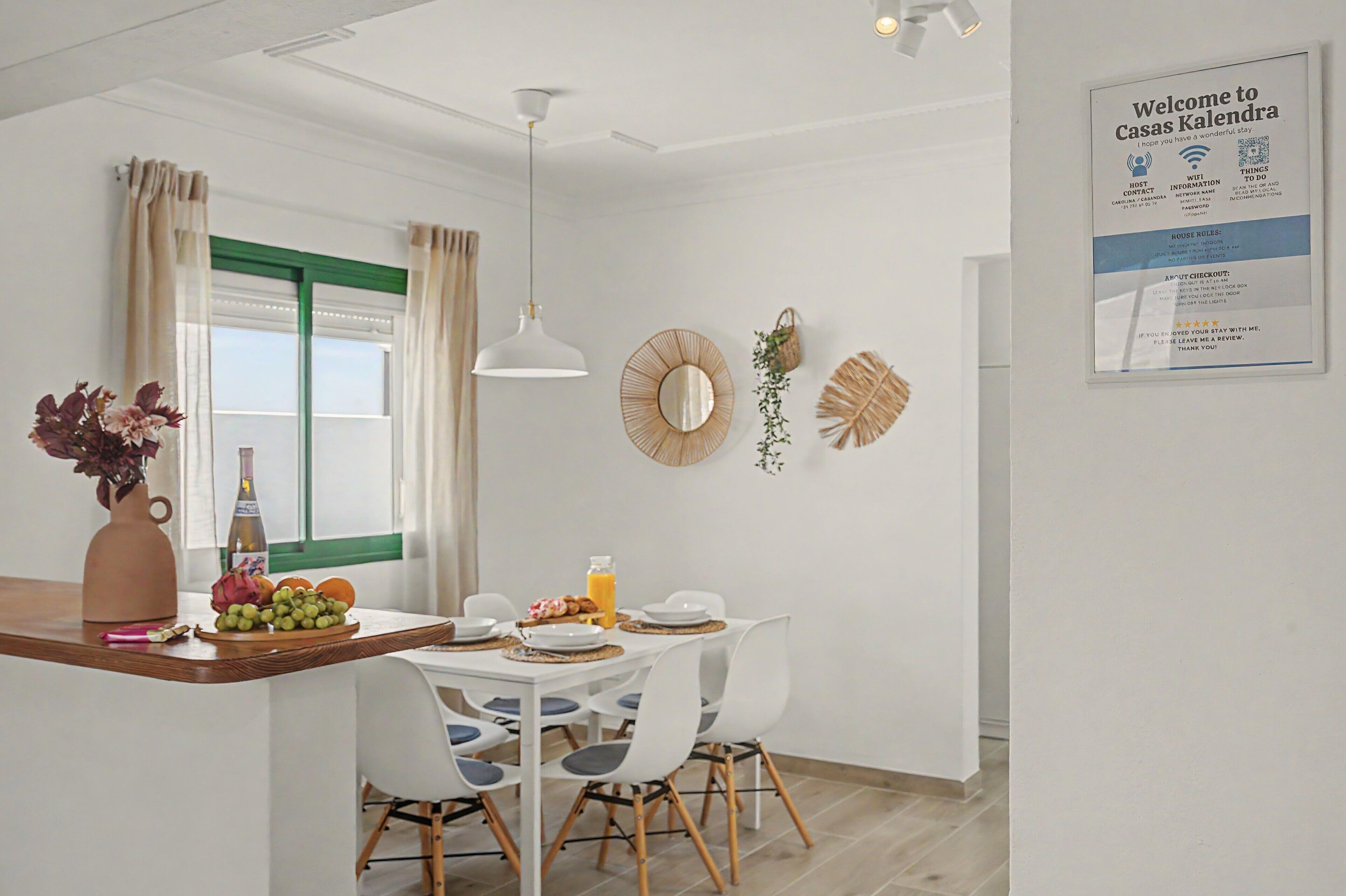 Une cuisine moderne avec un coin repas, un luminaire suspendu et un panneau d’accueil.