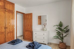 A bedroom with a bed, a dresser, a mirror, and a potted plant.