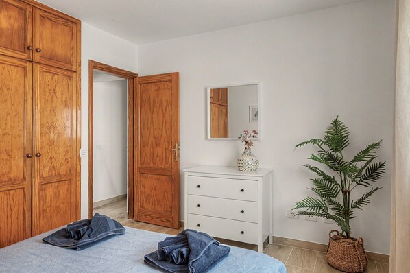 A bedroom with a bed, a dresser, a mirror, and a potted plant.