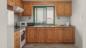 Une cuisine avec des meubles de rangement en bois, un four à micro-ondes, une cuisinière et une fenêtre dotée d’un cadre vert.