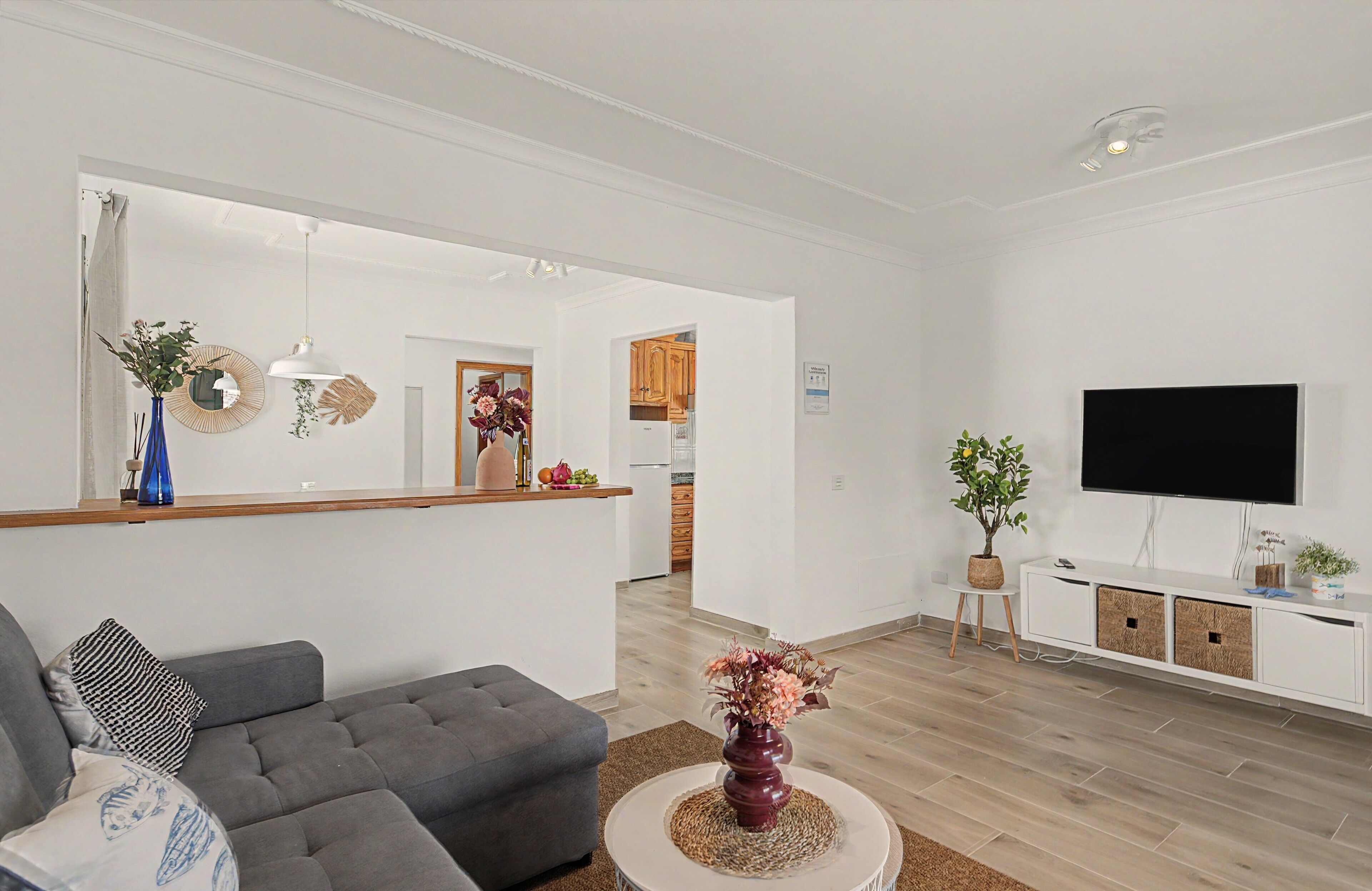 Een moderne woonkamer met een grijze bank, een ronde salontafel en een flatscreen televisie aan de muur.