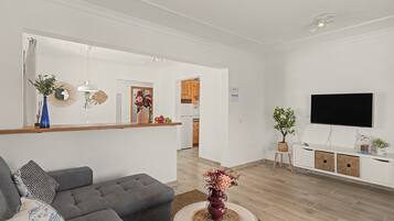 Een moderne woonkamer met een grijze bank, een ronde salontafel en een flatscreen televisie aan de muur.