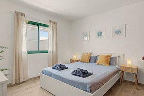Habitación de hotel con cama, dos mesitas de noche, ventana con cortinas y tres cuadros enmarcados en la pared.