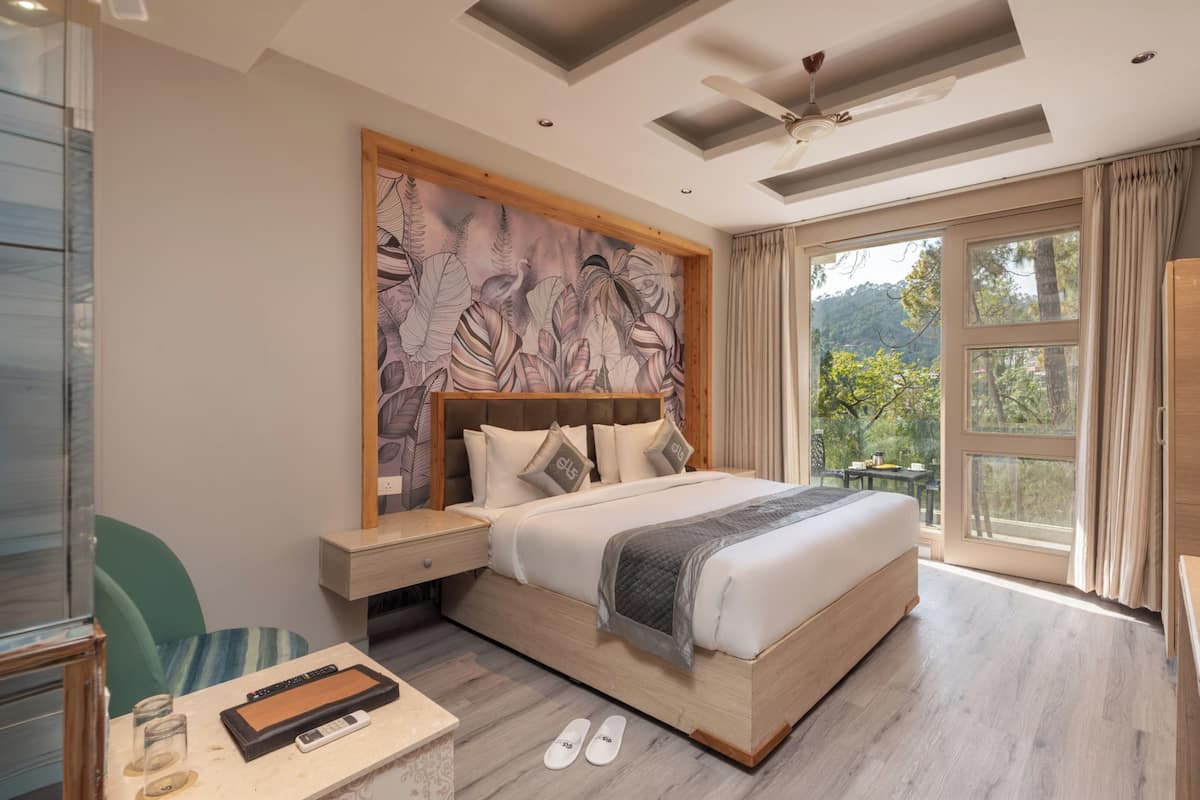 Une chambre moderne avec un grand lit, une table de chevet, un bureau avec une chaise et une vue sur l’extérieur.