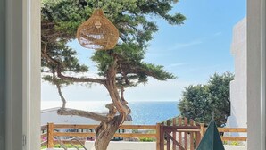 Une pièce avec vue sur un arbre et la mer, un luminaire suspendu et une console blanche agrémentée d’objets décoratifs.
