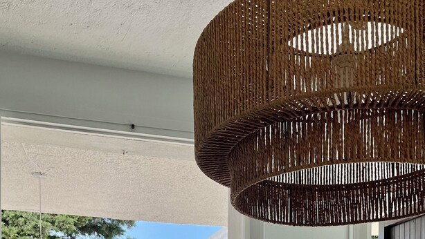 Un coin repas avec une table dressée pour deux personnes, une chaise en osier, un luminaire suspendu et une vue sur la mer.