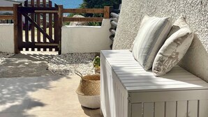 Un espace extérieur aménagé avec des sièges blancs, un mur en pierre, une porte en bois et une vue sur la mer.