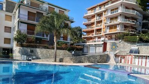 Une piscine bordée de pierres, entourée d’immeubles à plusieurs étages dotés de balcons et d’un palmier.