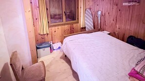 Una habitación de madera con una cama, una silla, una ventana con cortinas y una lámpara colgante.