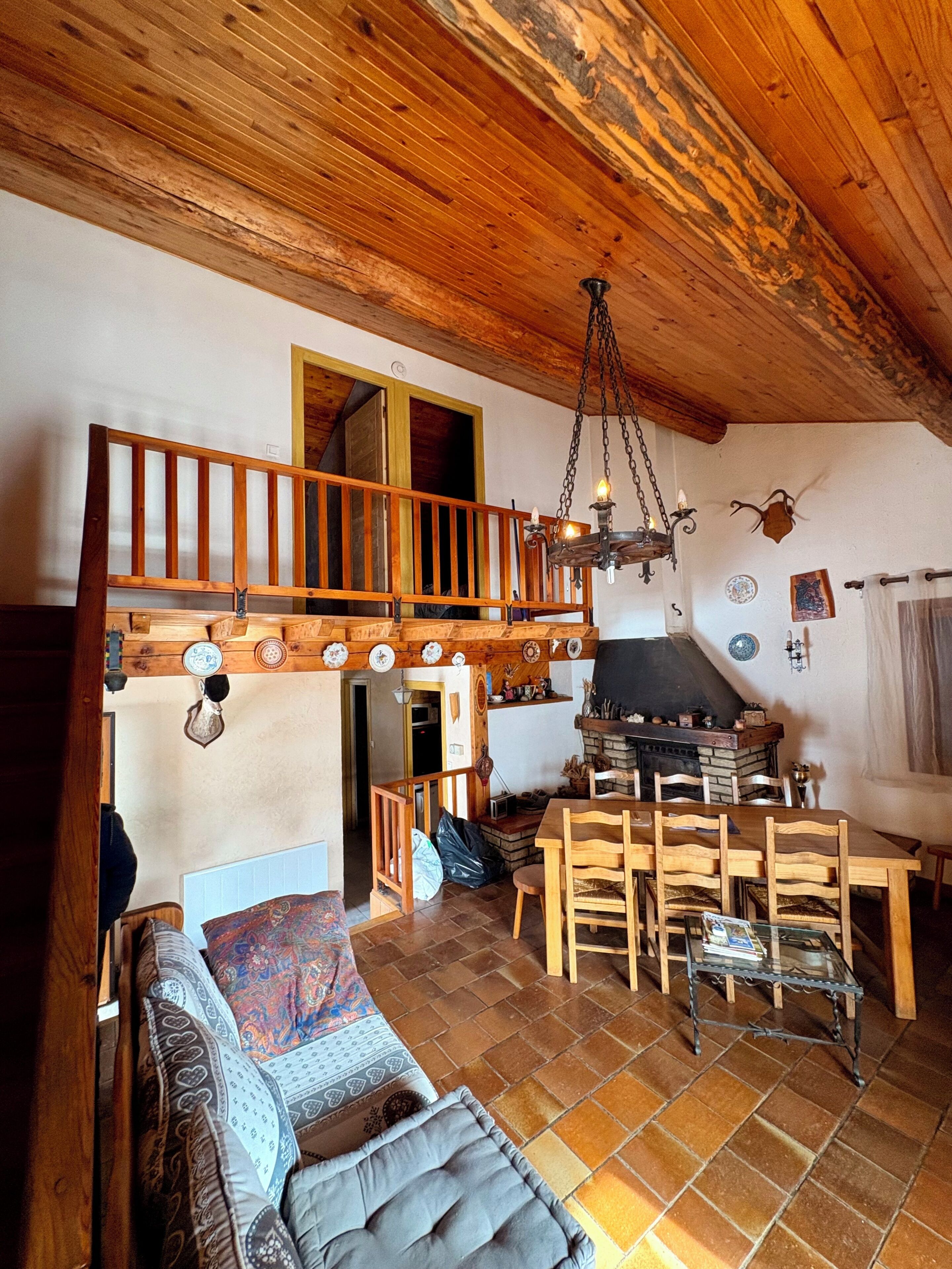 A rustic interior with a wooden staircase, a fireplace, a dining area, and a sofa.