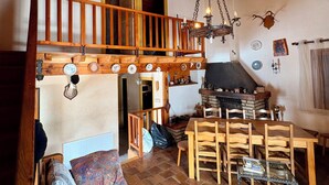 Un interior rústico con una escalera de madera, chimenea, zona de comedor y sofá.