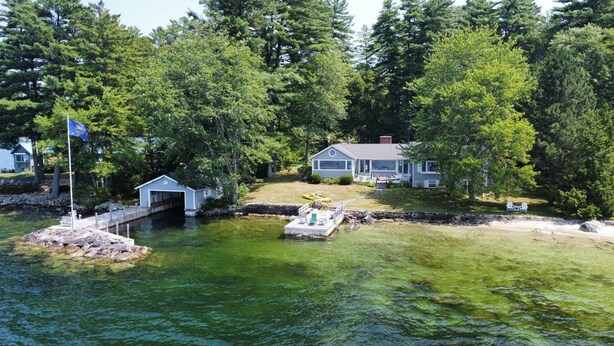 A lakeside cabin with a dock, a boathouse, and a house with a deck. - Exceptional Lakefront Home on Springfield Point – Lake Winnipesaukee (Wolfeboro)