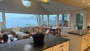 A kitchen with a large island, dining area with chairs, and large windows overlooking a body of water. - Exceptional Lakefront Home on Springfield Point – Lake Winnipesaukee (Wolfeboro)