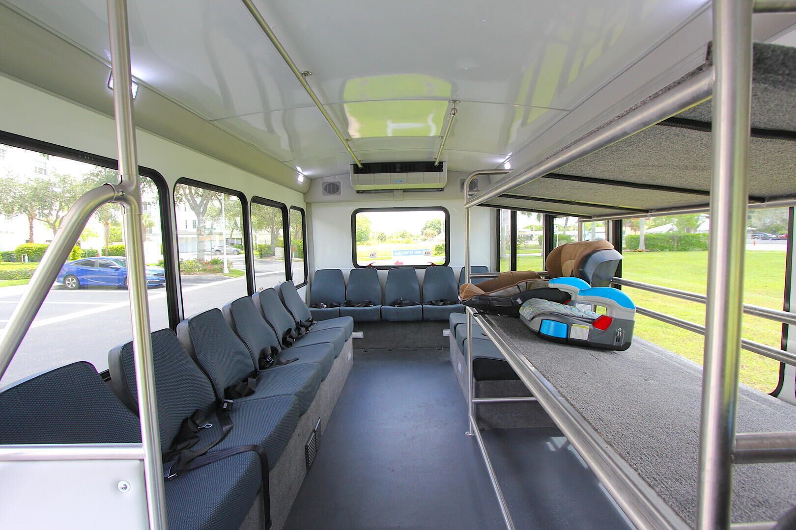 Interior de ônibus com fileiras de assentos, um bagageiro e janelas que mostram a rua.