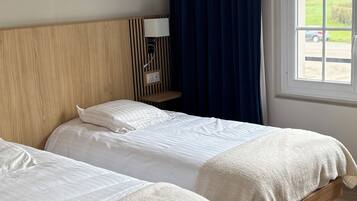 Habitación de hotel con dos camas, cabecera de madera, ventana con cortinas y vistas al exterior.