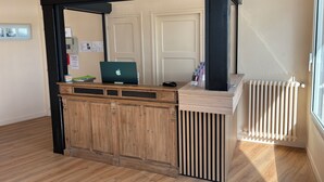 A reception desk with a laptop, a phone, and a magazine rack. - Hôtel L'Escale des Hayons (Esclavelles)
