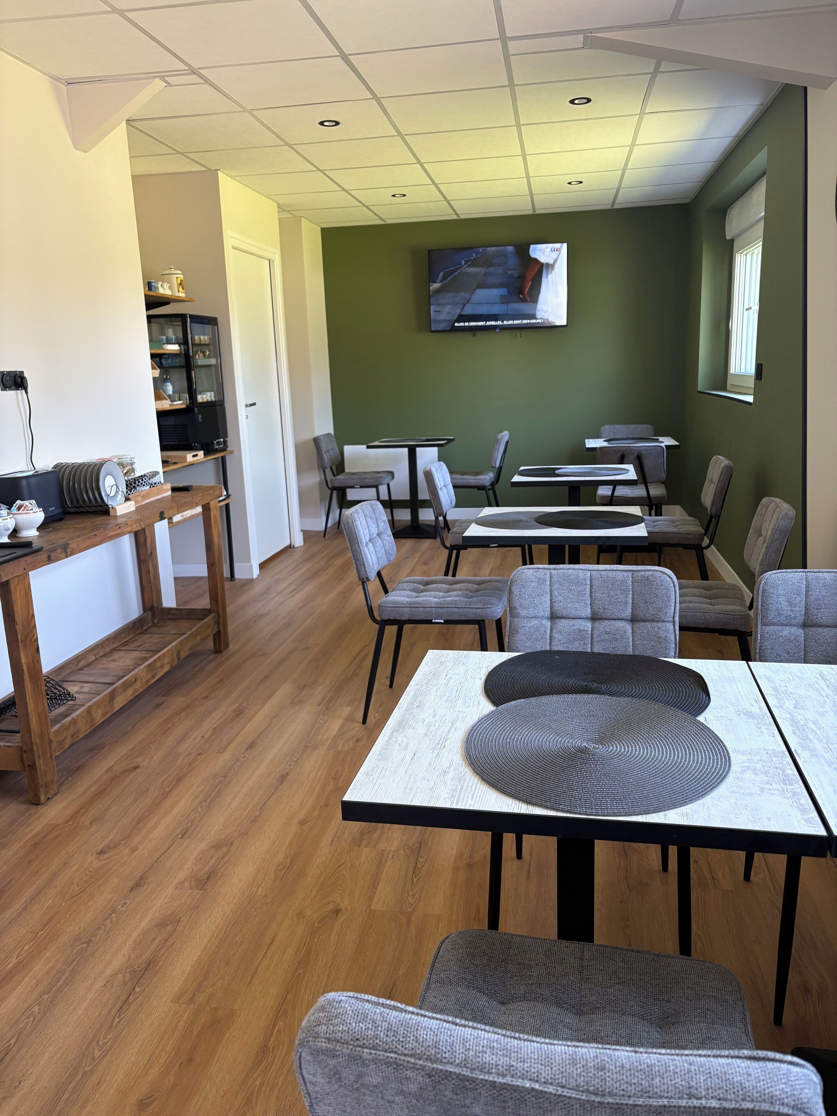 A dining area with tables and chairs, a television on the wall, and a wooden floor.