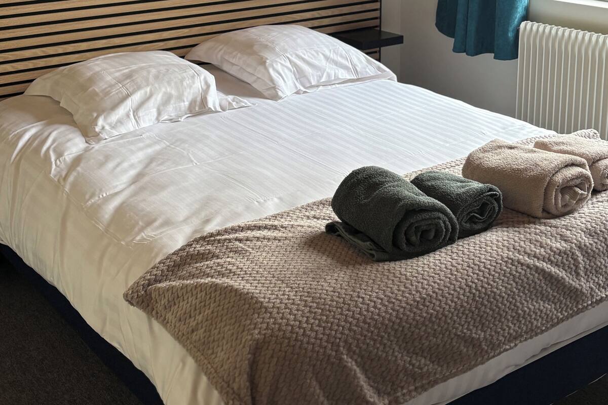 Ein Bett mit weißen Leinentüchern, einer gestrickten Decke und zusammengerollten Handtüchern.