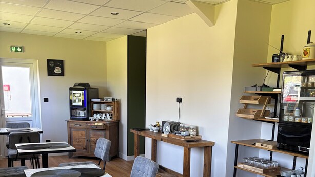 A dining area with tables, chairs, a coffee machine, and a refrigerator. - Hôtel L'Escale des Hayons (Esclavelles)