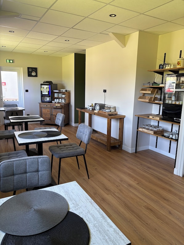 A dining area with tables, chairs, a coffee machine, and a refrigerator.