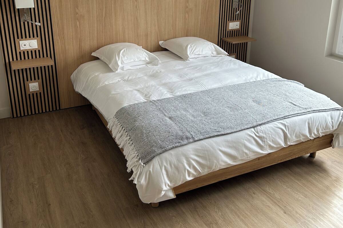 Ein Schlafzimmer mit einem Holzkopfende, einem Bett mit weißer Bettwäsche und einem Fenster rechts.