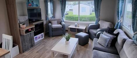 A modern living room with a sofa set, a TV, a coffee table, and a window with curtains.