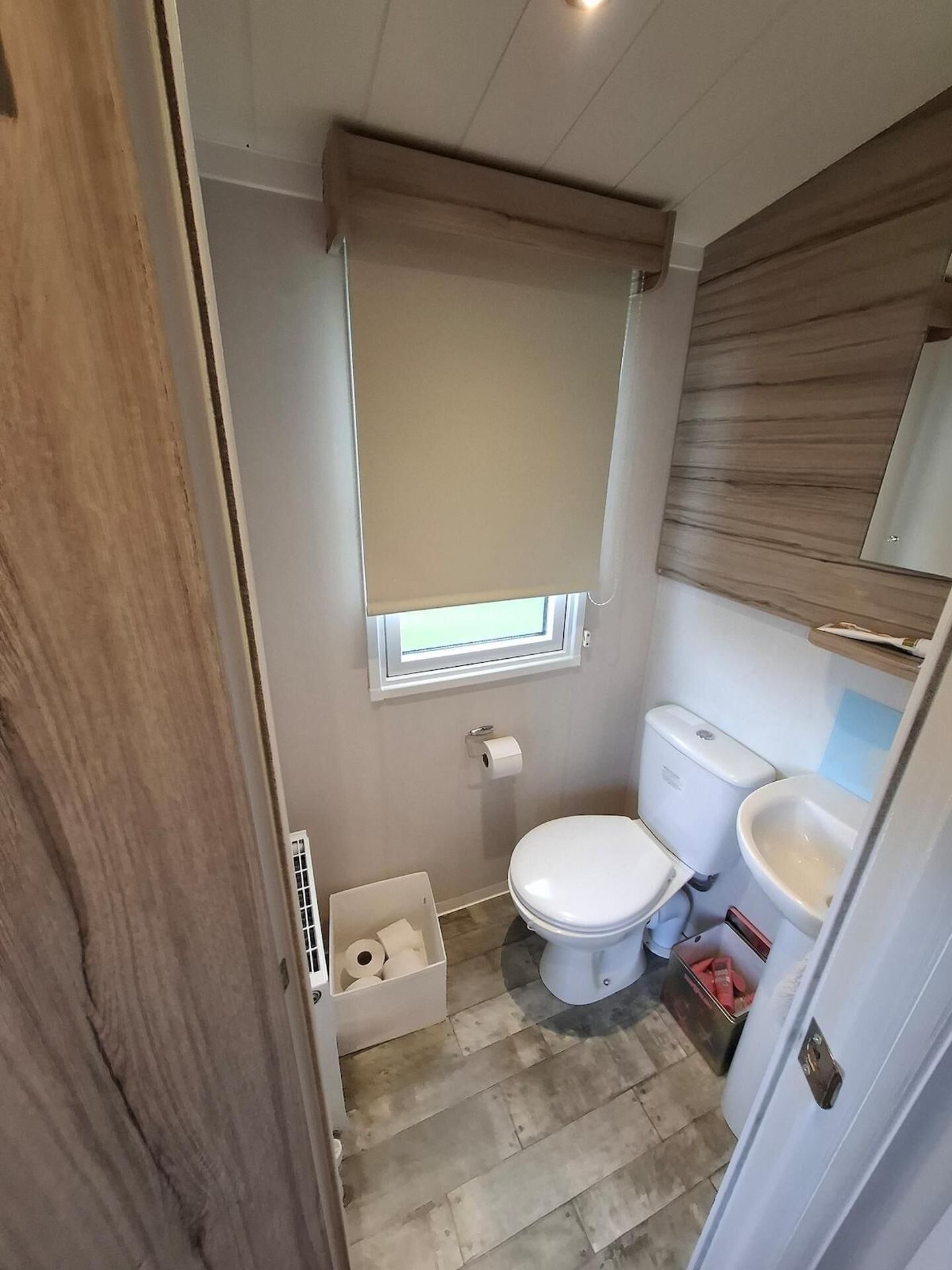 A compact bathroom with a toilet, bidet, and a small window with a beige blind.