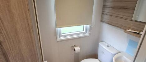 A compact bathroom with a toilet, bidet, and a small window with a beige blind.